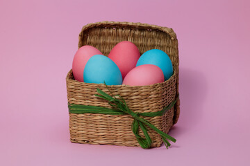 Colored Easter eggs in a square basket on a pink background. Easter