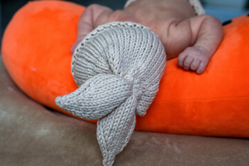 infant wears knitted rabbit hat with ears on head, baby sleeping on plush carrot