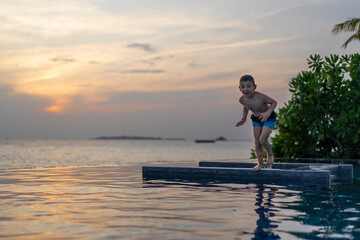 Little boy jumping from the side into the pool at sunset