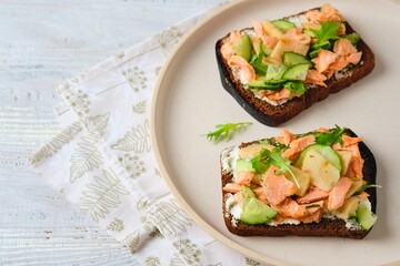 Smorrebrod, an open sandwich on rye bread with boiled salmon, fresh cucumber, cream cheese, apple and herbs on a ceramic plate on a light concrete background. Danish cuisine.