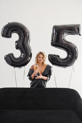 a naked blonde with tattoos in a black coat by a black sofa. birthday