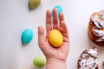 Human hand holds orange, deep yellow Easter egg on an white background with kraffin cake.