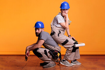Professional carpenters holding construction tools in studio shot, posing with working instruments. Team of constructors working with pair of pliers, painting roller and brush over background.