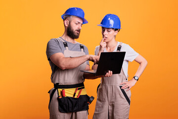Renovators team holding laptop and browsing internet online, discussing about renovation project. Construction workers using wireless pc to search building inspiration, studio shot.