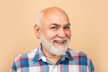 Obraz premium Happy old mature man smiling. Portrait of an bald old mature senior man with grey beard in shirt isolated on beige studio background.