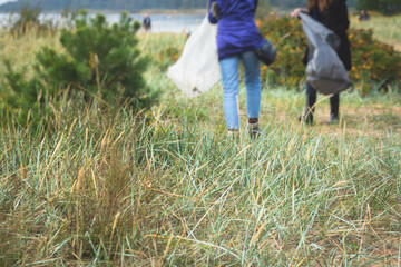 Team group of young people volunteering and participate in community work cleaning day at sandy beach, activists collecting waste, rubbish, garbage and litter in bags in the coast park together