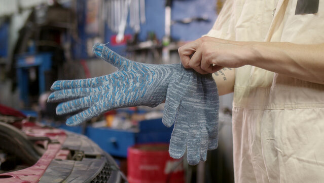 In car service, unrecognizable woman worker puts gray gloves on her hands and prepares for regular car maintenance work. Close up view of girl putting on gloves at work.