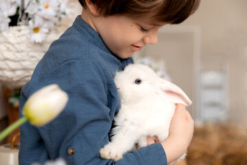 White Easter rabbit sits on the hands of a little boy, who huggs the rabbit
