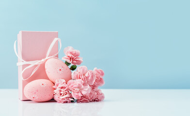 Fototapeta na wymiar Easter eggs with pink gift box and tender carnations spring flowers on white table blue background. Side view. Happy Easter in pink. Copy space