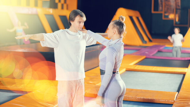 Middle Age Woman Trainer Instructing Young Man Doing Physical Exercises Before Jumping In Trampoline Arena