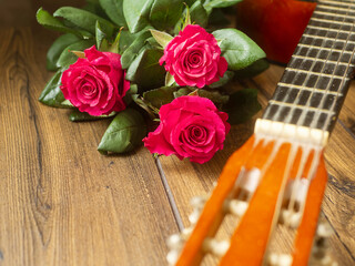 Classic acoustic guitar on a wooden floor and bouquet of red rosses. Expression of gratitude and love for great music performance. Romantic background.