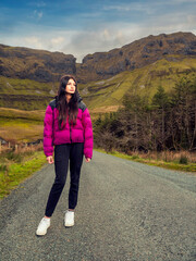 Young teenager girl posing on a road with beautiful scenery background. Gleniff Horse shoe drive, Ireland. Travel and tourism concept. The model is tall with dark hair and magenta jacket. Nature trip