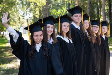 Row of happy young people in graduation gowns outdoors. Students in the park.