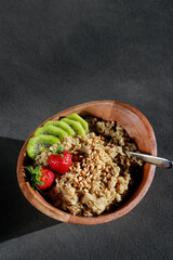 upper view of healthy homemade oatmeal in a wooden bowl with fruits on grey table