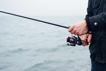 Spin fishing. Male hands hold a spinning rod against the background of the sea in spring, close-up, soft focus.