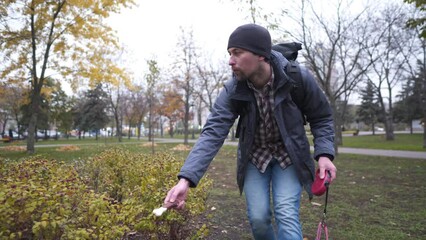 In search of lost domestic husky dog in city, adult Caucasian man calls puppy, attracting attention with treat for animals in city park in autumn cloudy weather. Responsible attitude to animals.