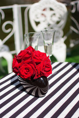 a bouquet of roses glasses of champagne on a tablecloth in black stripes on a round table