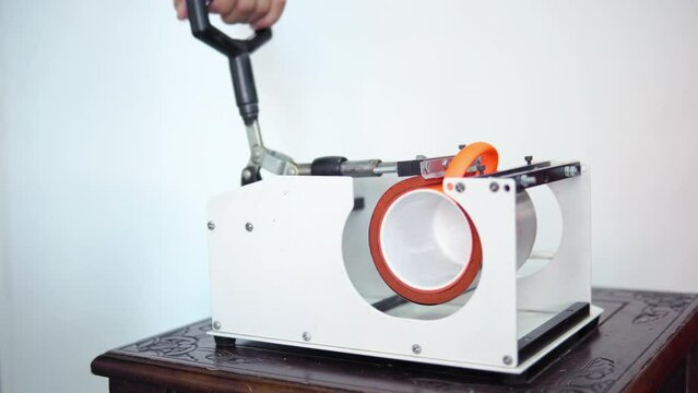 Man putting mug in a thermopress for cup print - intended for transfer image or a logo on a mug, cup