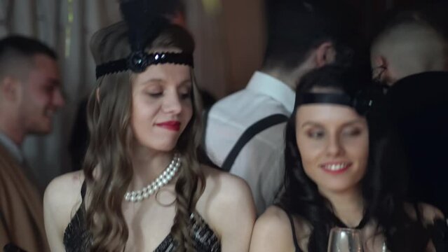 Vintage, retro Great gatsby (Roaring twenties) dressed women with smoking mouthpiece drinking champagne and dancing on a themed glamorous party