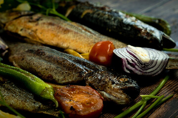 This close-up stock photo showcases a deliciously grilled with trout, sea bass, and sea bream skewered in the background with lemon slices and fresh herbs. 