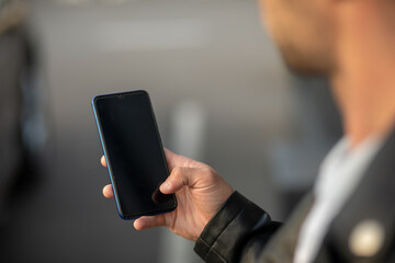 Closeup shot of an unrecognizable man holding mobile phone in hand, blurred background