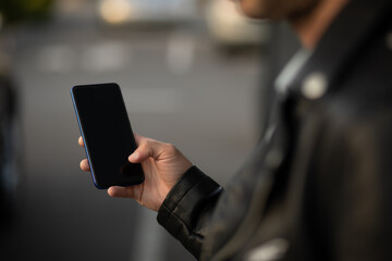 Closeup shot of an young modern man holding mobile phone in hand, blurred background