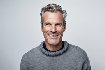 Obraz premium Portrait of handsome mature man in sweater smiling at camera over grey background