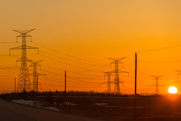 Fototapeta na wymiar Powerlines and pylons are silhouetted against the glow of the sunset sky 