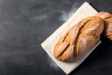 two freshly baked loaves, freshly baked bread on top of a tea towel on a black stone table