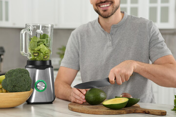 Fototapeta premium Man cutting avocado for delicious smoothie at white marble table in kitchen, closeup