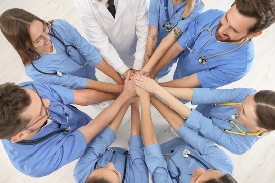 Doctor and interns stacking hands together indoors, top view