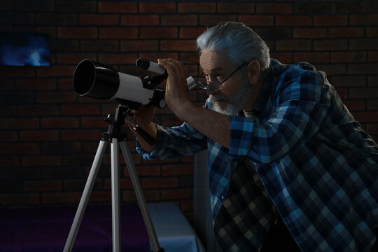 Senior Man Looking At Stars Through Telescope In Room