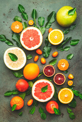 Citrus fruit food background, top view. Mix of different whole and sliced fruits: orange, grapefruit, tangerine and other with leaves on  green table