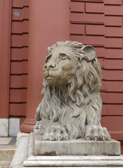 Red public building, with a lying lion statue guarding the entrance.