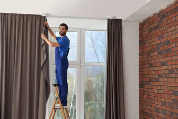 Obraz na płótnie Canvas Worker in uniform hanging window curtain indoors