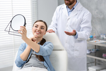 Obraz premium Young woman looking at her new dental implants in mirror indoors