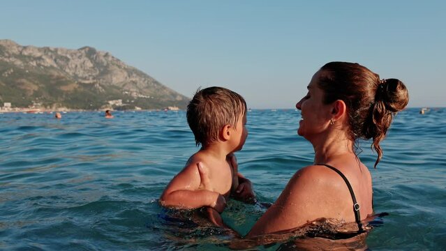 Cheerful mother plays with her son in the sea