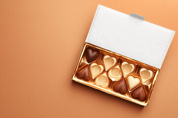 Partially empty box of chocolate candies on light brown background, top view. Space for text