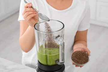 Woman adding chia seeds into blender with delicious smoothie in kitchen, closeup