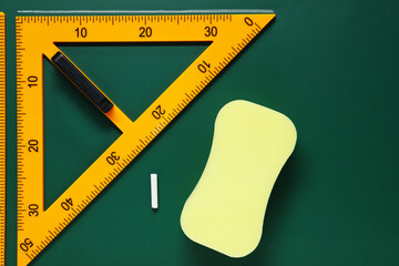 Protractor, sponge, chalk and ruler on green chalkboard, flat lay