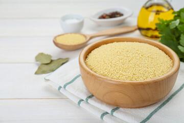 Bowl of raw couscous on white wooden table, closeup. Space for text