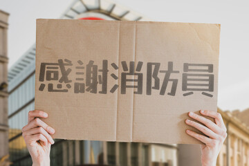 The phrase " Thank you firefighters " on a banner in men's hands with blurred background. Heroes. Hard job. Rescuers. Rescue. Dangerous. Respect. Honor. Support. Essential workers