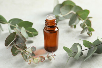 Bottle of eucalyptus essential oil and leaves on white table