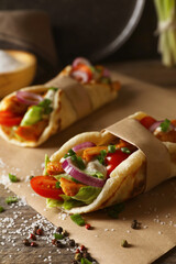 Fototapeta na wymiar Delicious pita wraps with meat and vegetables on wooden table, closeup