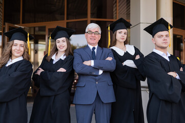 A professor and his students in graduation gowns stand with their arms crossed over their chests.