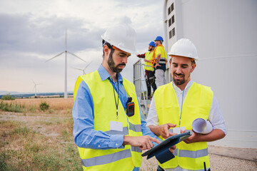 group of wind mill professional engineers contractors working and using a tablet to watch the draft of the construction of the generator propeller of renewable energy wearing helmet and safety vest