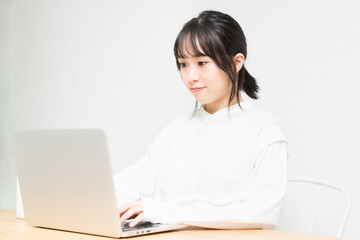 白背景の前でPCを操作する若い女性