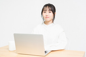 白背景の前でPCを操作する若い女性