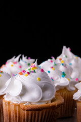 Fototapeta na wymiar Fluffy vanilla cupcakes, with meringue and dragees on a black background.