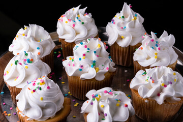 Fluffy vanilla cupcakes, with meringue and dragees on a black background.
